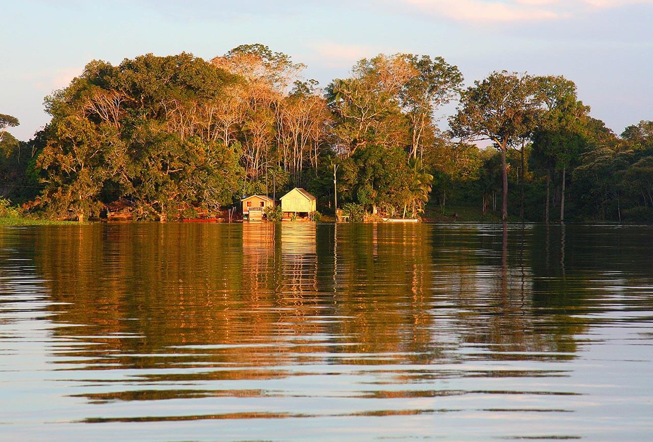 imagem mostra rio e algumas casas cercadas por árvores ao fundo. Retrato da pandemia na Amazônia