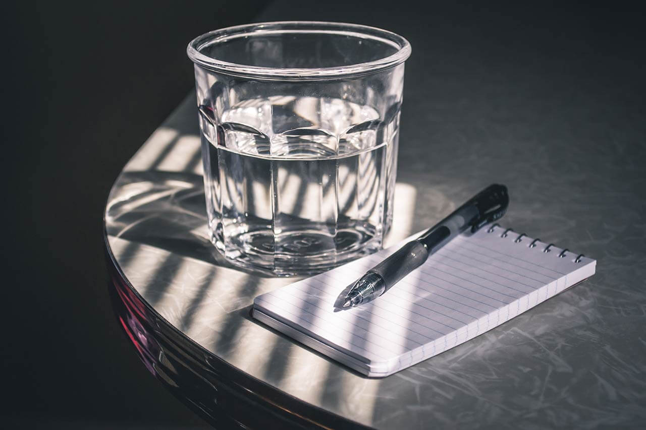 imagem mostra um copo de água e um bloco de papel com uma caneta em cima para representar o encontro realizado sobre Água, Inovação e Urbanização